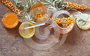 Vitamin healthy sea buckthorn tea in a glass cup with a teapot, honey, jam, fresh raw sea buckthorn berries and twigs on a wooden