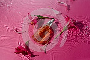 Vitamin narutal serum in a glass bottle in water surrounded by flowers on pink