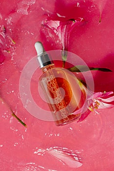 Vitamin narutal serum in a glass bottle in water surrounded by flowers on pink