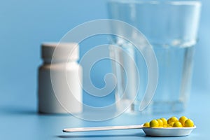 Vitamin or pharmaceutical pills in a white spoon on the background of a glass glass with water and a white medicine bottle. Food