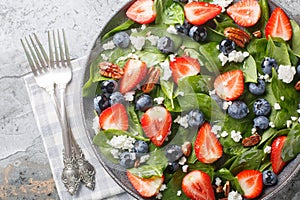 Vitamin salad of fresh spinach, strawberries and blueberries with cheese and pecans with honey dressing close-up in a plate.