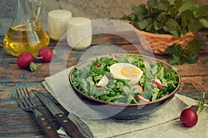 Vitamin salad from lettuce, radish, green onions and eggs, seasoned with vegetable oil in plate on wooden background. Healthy food