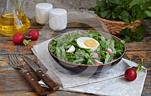 Vitamin salad from lettuce, radish, green onions and eggs, seasoned with vegetable oil in plate on wooden background. Healthy food