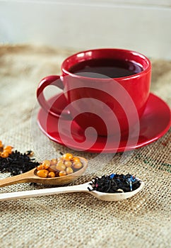 Vitaminic healthy black tea with sea buckthorn in red cup with fresh raw sea buckthorn berries and black tea in wooden spoons