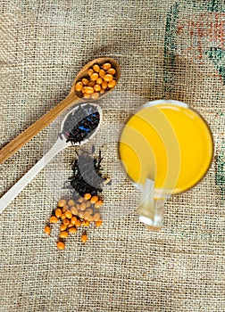 Vitaminic healthy sea buckthorn tea in small cup with fresh raw sea buckthorn berries and black tea in wooden spoons