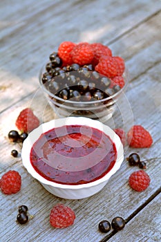 Vitaminic, red jam of home blackcurrant and red raspberry in white plate neat glass plate with full berries on wooden texture