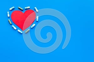 Vitamins of drugs for heart. Color pills near heart sign on blue background top view space for text