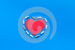 Vitamins of drugs for heart. Color pills near heart sign on blue background top view space for text