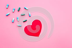 Vitamins of drugs for heart. Color pills near heart sign on pink background top view copy space
