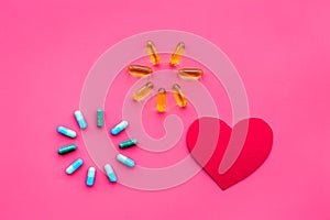 Vitamins of drugs for heart. Color pills near heart sign on pink background top view copy space