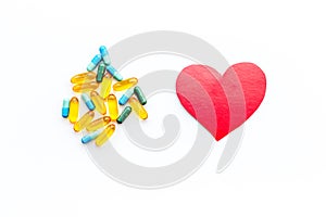 Vitamins of drugs for heart. Color pills near heart sign on white background top view copy space