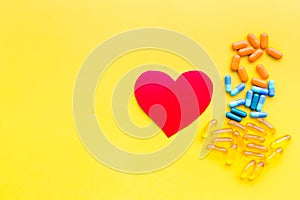 Vitamins of drugs for heart. Color pills near heart sign on yellow background top view space for text