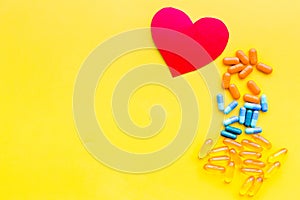 Vitamins of drugs for heart. Color pills near heart sign on yellow background top view space for text