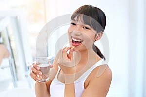 Vitamins keep you healthy and strong. Portrait of a cheerful attractive young woman taking medication at home during the