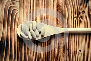 Vitamins or supplements in wooden spoon on vintage wooden board