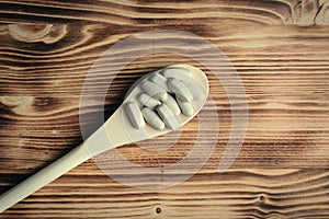 Vitamins or supplements in wooden spoon on vintage wooden board