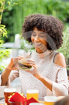 Vivacious happy young black woman eating a hamburger
