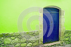 Vivid blue wooden closed door on vibrant lime green stone wall