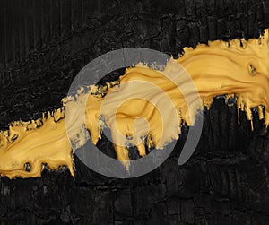 Vivid contrast black and gold in abstract background of metallic gold paint swirling over charred black ashes