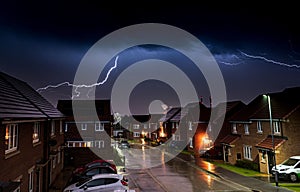 Vivid lightning strike illuminating an urban landscape at night, featuring houses and cars