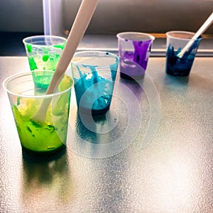 Vivid liquid acrylic paint in different colors mixed inside small plastic cups