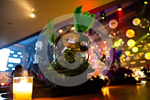 Vivid Mardi Gras masks with feathers on a glittering tinsel base, lit by candles on a wooden table at a festive event venue