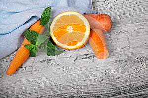 Vivid orange, slices of carrot and sappy green leaves of mint on a light wooden background.