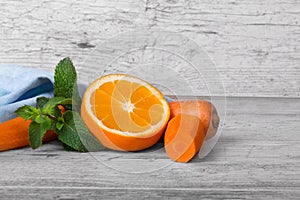 Vivid orange, slices of carrot and sappy green leaves of mint on a light wooden background.
