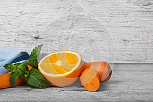 Vivid orange, slices of carrot and sappy green leaves of mint on a light wooden background.