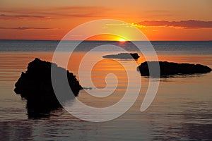 Vivid orange sunset over water, with rock silhouettes