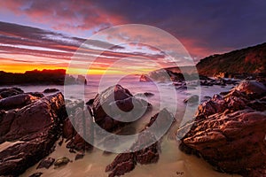 Vivid red sunrise over rocky beach coast