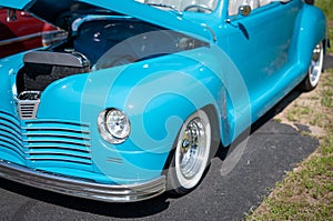 Vivid sky blue antique vintage convertible automobile with top down and open hood at a car show in Minnesota in bright sunlight. I