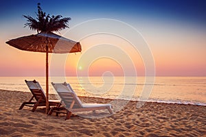 Vivid sunrise on a beautiful sandy beach and sunshade photo