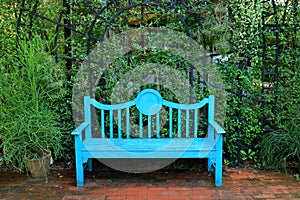 Vivid turquoise blue colored wooden bench on the terracotta brick pathway in green garden