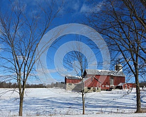 Vivid vintage red barn on hillside in winter snow under deep blue sky above