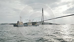 Vladivostok Bridge. View from a moving ferry at sunset with a ship in the background.