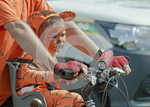 girl disguised as a tiger cub, sits on her father`s bike