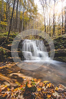 Vlasky River with waterfall illuminated with sun in an untouched landscape in the middle of an autumn mixed forest in red-orange