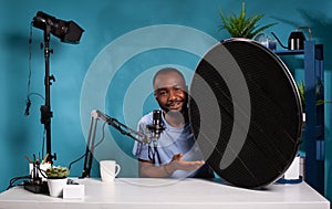 Vlogger explaining features of studio flash light modifier sitting at desk with microphone photo