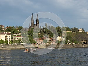 Vltava river bank with small ferry boat and historical fort Vysehrad with Basilica of St. Peter and Paul, gothic