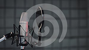 A vocal microphone and pop filter for singing or recording a podcast in a home music studio. Pan shot of a professional microphone