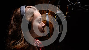 A vocalist sings into a studio microphone with headphones on her head, live performance, vocals, vocal studio, recording a track.