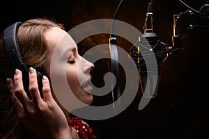 A vocalist sings into a studio microphone with headphones on her head, live performance, vocals, vocal studio, recording a track.