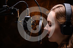 A vocalist sings into a studio microphone with headphones on her head, live performance, vocals, vocal studio, recording a track.