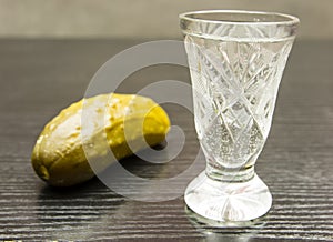 Vodka in a crystal glass and pickled cucumber.