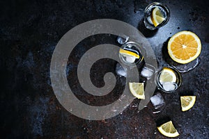 Vodka in glasses with lemon and ice. On the black stone table. Copyspace.