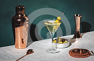 Vodka martini, classic alcoholic cocktail drink with vodka and vermouth, green olives garnish, dark background, bright hard light