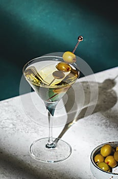 Vodka martini, classic alcoholic cocktail drink with vodka and vermouth, green olives garnish, dark background, bright hard light