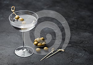 Vodka martini gin cocktail in modern glass with olives in metal bowl and bamboo sticks on black
