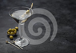 Vodka martini gin cocktail in original glass with olives in metal bowl and bamboo sticks on black